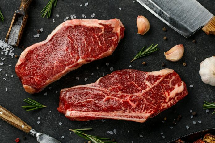 Photo by Sergey Kotenev two steaks on a cutting board next to garlic, garlic, and a knife