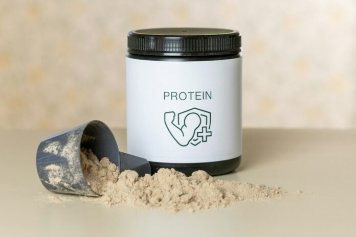 Photo by Aleksander Saks a jar of protein powder next to a scoop of powder